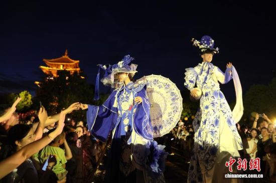7月30日晚,游客在江西景德镇陶阳里历史文化旅游区内与穿着青花瓷服饰的高跷演员互动。中新社记者 刘占昆 摄 7月30日晚,游客在江西景德镇陶阳里历史文化旅游区内与穿着青花瓷服饰的高跷演员互动。中新社记者 刘占昆 摄